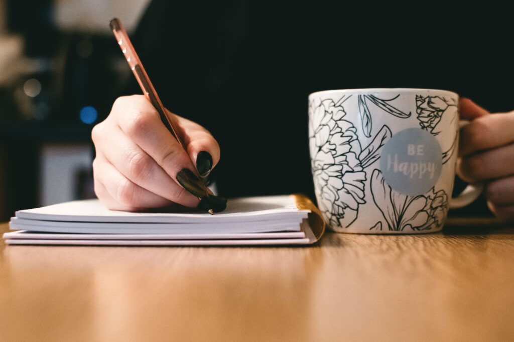 someone writing on a notebook and drinking something out of a cup